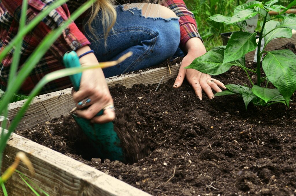 Person lockert die Erde in einem Hochbeet mit einer Schaufel