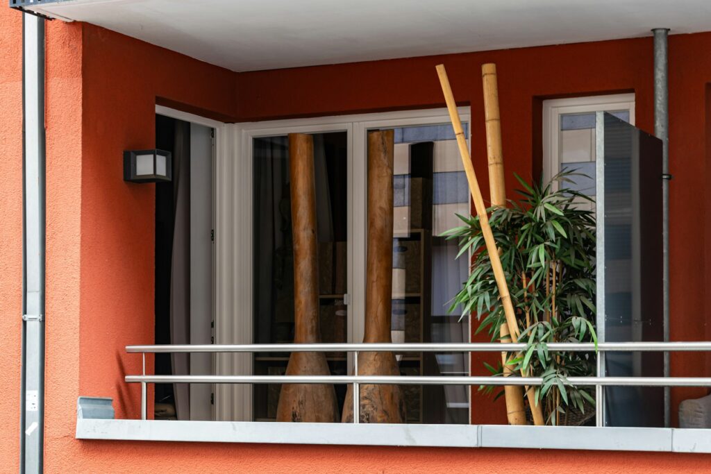 Balkon mit orangefarbener Wand, weißem Geländer und Bambus im Kübel