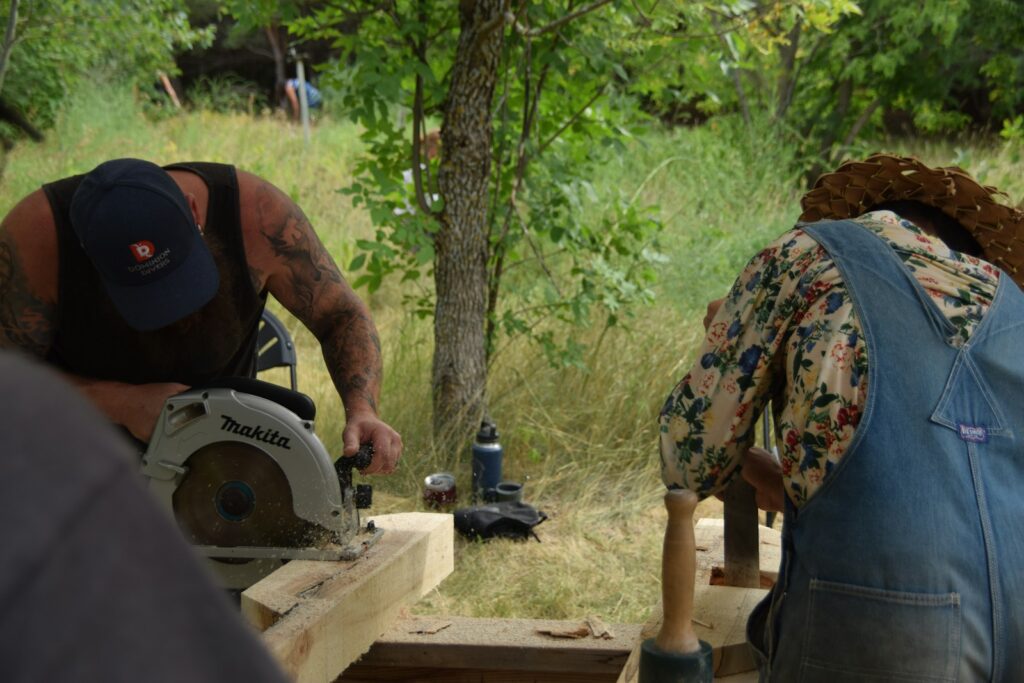 Mann sägt im Freien mit einer Kreissäge einen Holzbalken zu – Vorbereitung, um ein Gartenhaus selber bauen zu können