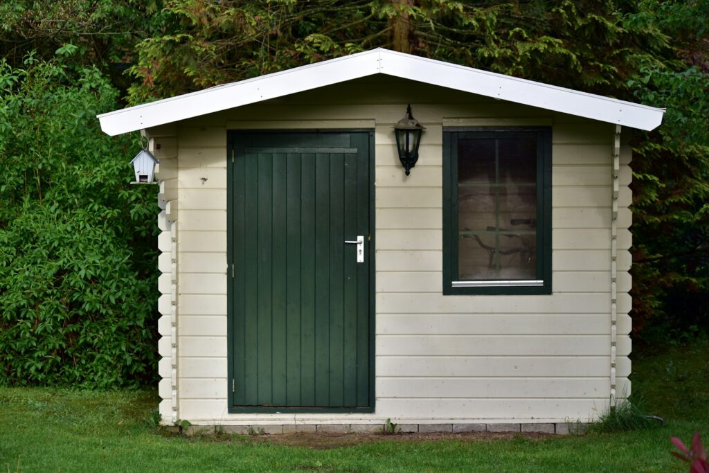Kleines Holzhaus mit grüner Tür und Fenster im Garten – so kann es aussehen, wenn du ein Gartenhaus selber bauen willst