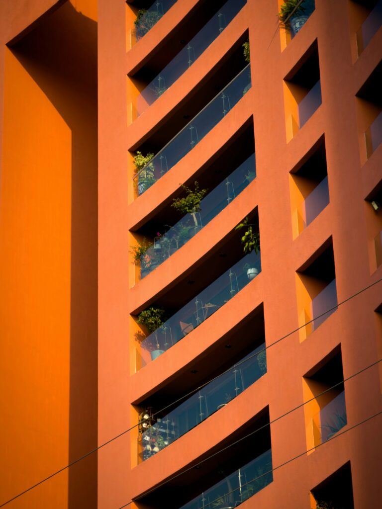Orange Fassade mit Glasbrüstungen und Topfpflanzen, ein fester Windschutz Balkon aus Glas